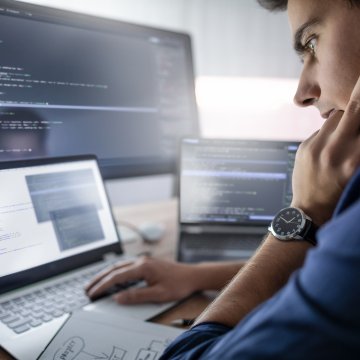 Guy looking at computer code on a screen at a desk.